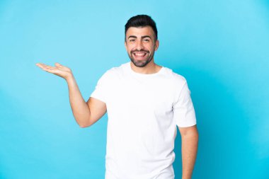 İzole edilmiş mavi arka plan üzerinde beyaz bir adam bir ilan vermek için avucunun içinde hayali bir mekan tutuyor.