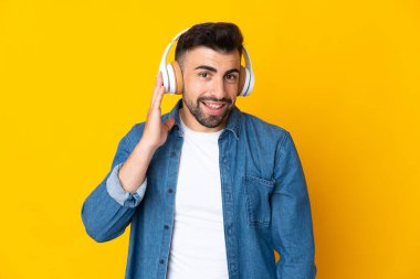İzole edilmiş sarı arka planda beyaz bir adam müzik dinliyor.
