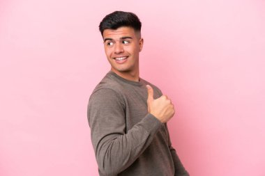 Pembe arka planda izole edilmiş beyaz, yakışıklı genç bir adam bir ürün sunmak için kenarı işaret ediyor.