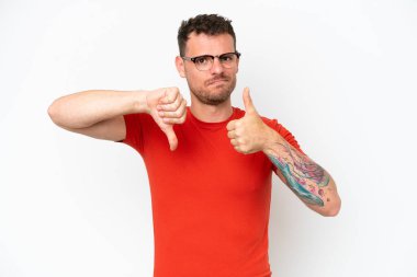 Beyaz arka planda izole edilmiş beyaz tenli yakışıklı bir adam iyiye-kötüye işaret yapıyor. Evet ya da hayır arasında kararsız