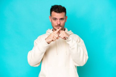 Mavi arka planda izole edilmiş beyaz, yakışıklı genç bir adam sessizlik işareti gösteriyor.