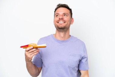 Beyaz arka planda saşimi tutan genç beyaz bir adam yukarı bakarken bir fikir düşünüyor.