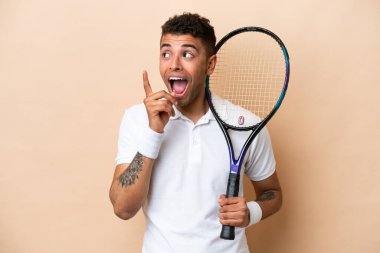 Bej arka planda tenis oynayan genç Brezilyalı yakışıklı bir adam çözümü bulmak için parmağını kaldırıyor.