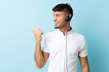 Kolombiyalı tele pazarlamacı, izole edilmiş arka planda çalışan bir kulaklıkla bir ürünü sunmak için kenarı işaret ediyor.