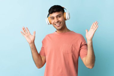Mavi arka planda izole genç Kolombiyalı adam şaşırdı ve müzik dinliyor