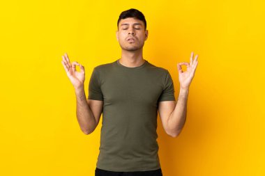Zen pozisyonunda sarı arka planda izole genç Kolombiyalı adam