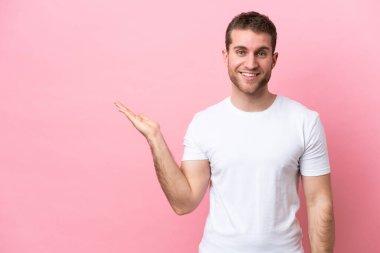 Pembe arka planda izole edilmiş genç beyaz bir adam bir ilan vermek için avucunun içinde hayali bir fotokopi makinesi tutuyor.