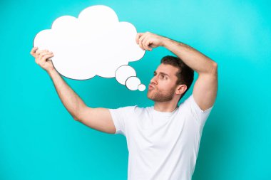 Young caucasian man isolated on blue background holding a thinking speech bubble