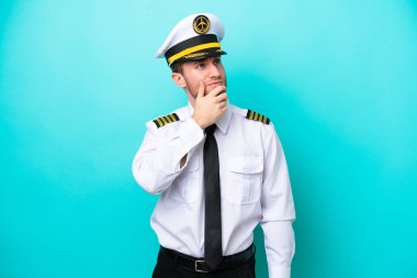 Kafkasyalı uçak pilotu mavi arka planda izole edilmiş. Şüpheleri var ve kafası karışmış bir yüz ifadesi var.