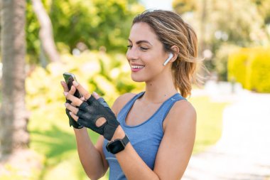 Açık havada giyinen ve telefonlu müzik dinleyen genç sarışın kadın.