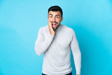 Kafkasyalı, mavi arka planda, şaşırmış ve şok olmuş bir yüz ifadesi var.