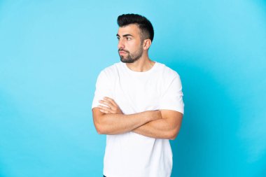 İzole edilmiş mavi arka planda beyaz bir adam kollarını çapraz tutuyor.