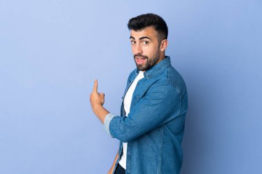 İzole edilmiş mavi arka planda beyaz bir adam geriye doğru işaret ediyor.