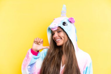 Sarı arka planda izole edilmiş tek boynuzlu at pijaması giyen beyaz bir kadın gururlu ve kendini beğenmiş.