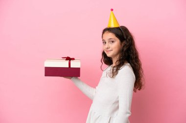 Küçük beyaz kız pembe arka planda izole edilmiş bir hediye tutuyor.