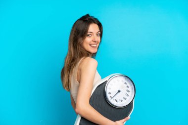 Genç beyaz kadın, mavi arka planda, tartı makinesiyle izole edilmiş.