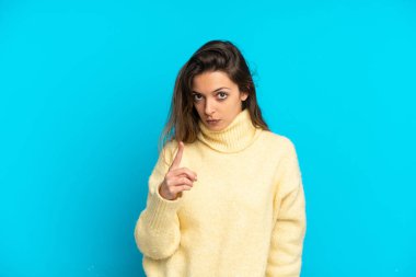 Mavi arka planda izole edilmiş genç beyaz kadın hayal kırıklığına uğramış ve ön tarafı işaret ediyor.