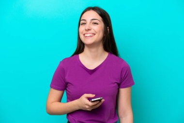 Genç kız mavi arka planda cep telefonu kullanarak izole edildi