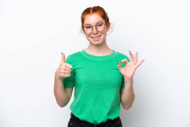 Beyaz arka planda izole edilmiş genç kızılımsı kadın işaret ve baş parmak işareti gösteriyor.