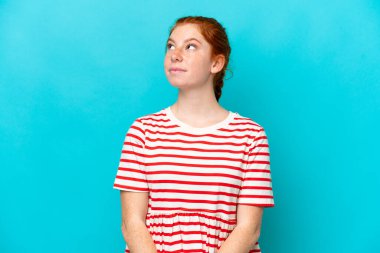 Kırmızımsı genç kadın mavi arka planda izole edilmiş ve yukarı bakıyor.