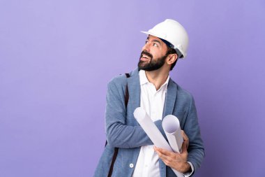 Miğferli genç bir mimar. Elinde mor bir arka plan var. Gülümserken yukarı bakıyor.