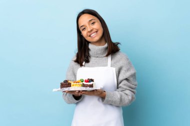Pasta şefi, mavi arka planda büyük bir pasta tutarak avuç içlerini bir arada tutuyor. İnsan bir şey ister..
