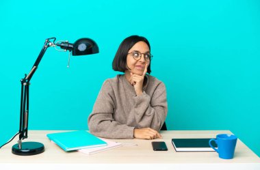 Genç öğrenci melez kadın masada ders çalışıyor ve düşünüyor.