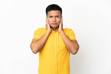 Beyaz arka planda izole edilmiş genç Ekvadorlu adam hayal kırıklığına uğramış ve kulaklarını kapatmış.