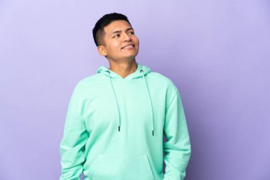 Genç Ekvadorlu bir adam mor arka planda izole edilmiş, yukarı bakarken bir fikir düşünüyor.