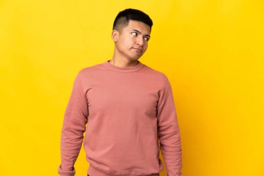 Sarı arka planda izole edilmiş genç Ekvadorlu adam şüpheli hareketler yapıyor.