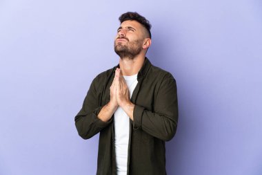 Caucasian man isolated on purple background keeps palm together. Person asks for something