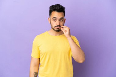 Mor arka planda izole edilmiş genç beyaz bir adam sessizlik işareti gösteriyor.