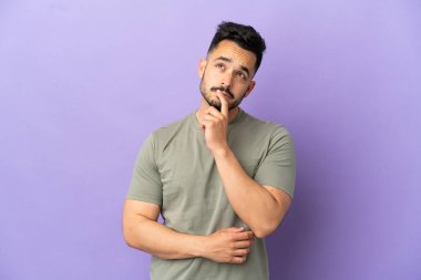 Mor arka planda izole edilmiş genç beyaz adam yukarı bakarken şüphe duyuyor.