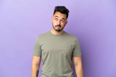 Mor arka planda izole edilmiş genç beyaz adam yukarı bakarken şüphe duyuyor.