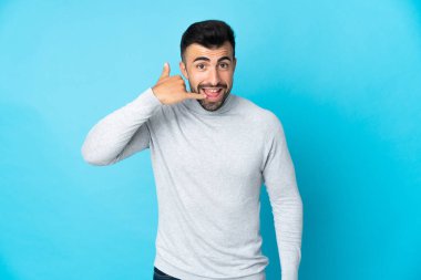 İzole edilmiş mavi arka planda beyaz bir adam telefon jesti yapıyor. Bana geri dönüş işareti ver.