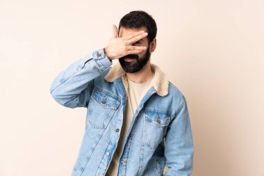 İzole edilmiş arka planda sakallı, gözleri elleriyle kaplayan ve gülümseyen beyaz bir adam.