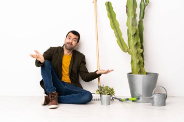 Bahçıvan içeride yerde oturuyor. Şüpheleri var ve ellerini kaldırıyor.