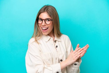 Mavi arka planda, gözlüklü ve alkışlayan genç beyaz kadın.