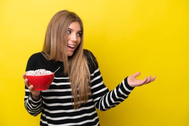 Sarı arka planda yalıtılmış bir kase mısır gevreği tutan beyaz bir kadın.