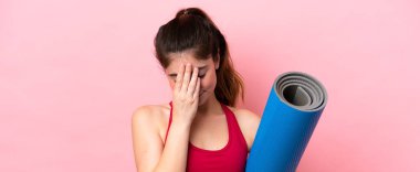 Genç sporcu kadın yoga derslerine giderken elinde yorgun ve hasta bir ifadeyle paspas tutuyor.