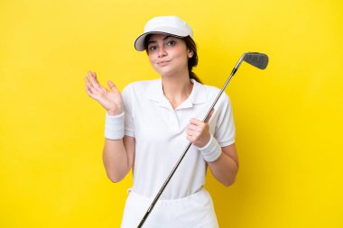 Sarı arka planda golf oynayan genç beyaz kadın el kaldırırken kuşkuları var.