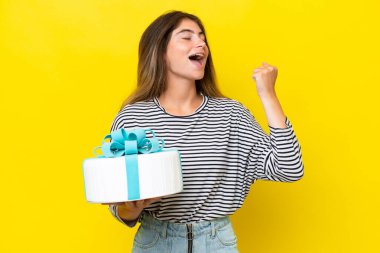 Young caucasian woman holding birthday cake isolated on yellow background celebrating a victory