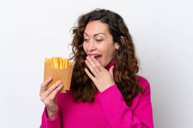 Beyaz arka planda izole edilmiş, şaşırmış ve şok olmuş bir yüz ifadesiyle patates kızartması yakalayan beyaz bir kadın.