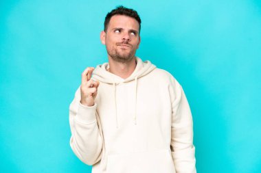 Beyaz tenli yakışıklı adam mavi arka planda izole edilmiş, şans diliyor ve en iyisini diliyor.