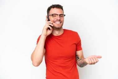 Beyaz arka planda izole edilmiş beyaz tenli yakışıklı bir adam cep telefonuyla sohbet ediyor.