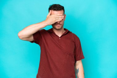 Beyaz tenli yakışıklı bir adam mavi arka planda tek başına, gözleri elleriyle kapatıyor. Bir şey görmek istemiyorum.