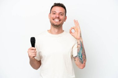 Beyaz arka planda izole edilmiş bir mikrofonu kaldıran beyaz tenli şarkıcı parmaklarıyla tamam işareti gösteriyor.