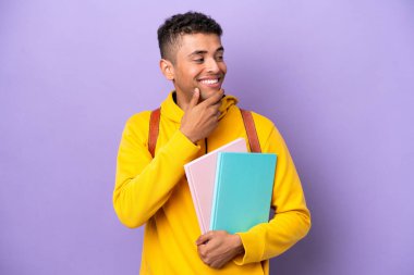 Mor arka planda izole edilmiş Brezilyalı genç bir adam yana bakıyor ve gülümsüyor.