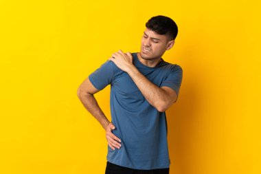Genç Kolombiyalı adam sarı arka planda izole edilmiş, omuz ağrısı çekiyor, çabaladığı için.