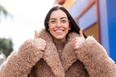 Genç esmer kadın açık havada gözlüklü ve başparmağıyla